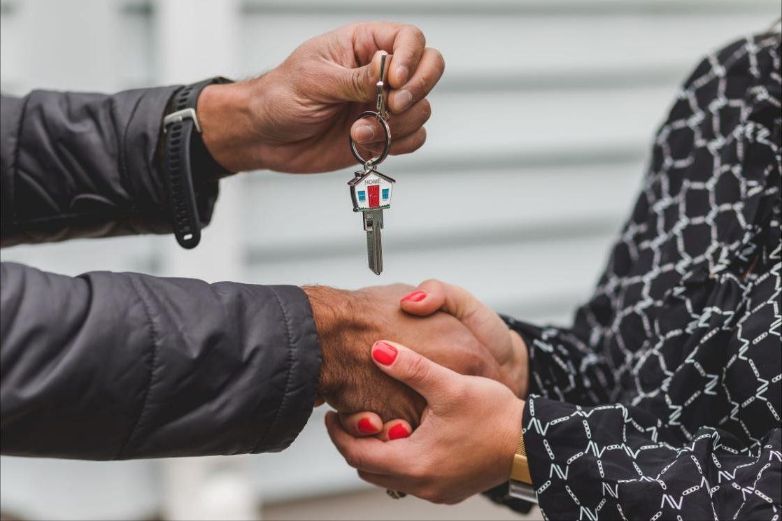 Close-up of a set of house keys with a house-shaped keyring being handed over during a handshake