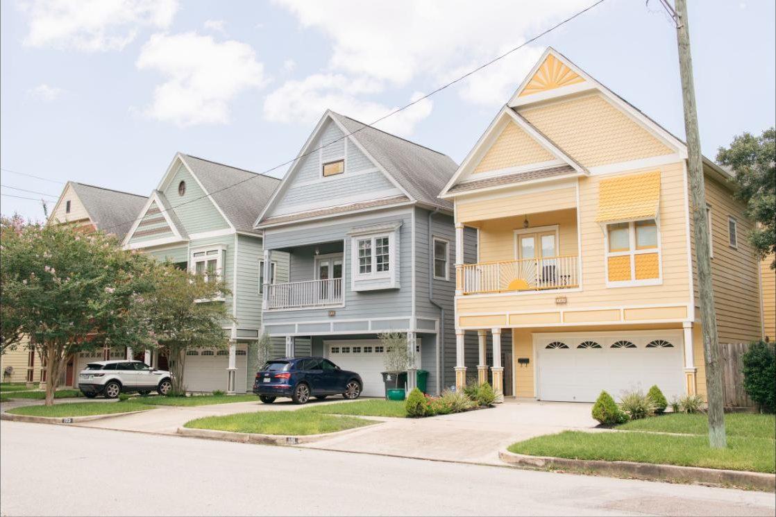 Row of colourful two-storey homes with front porches and gabled roofs on a street in Houston Heights