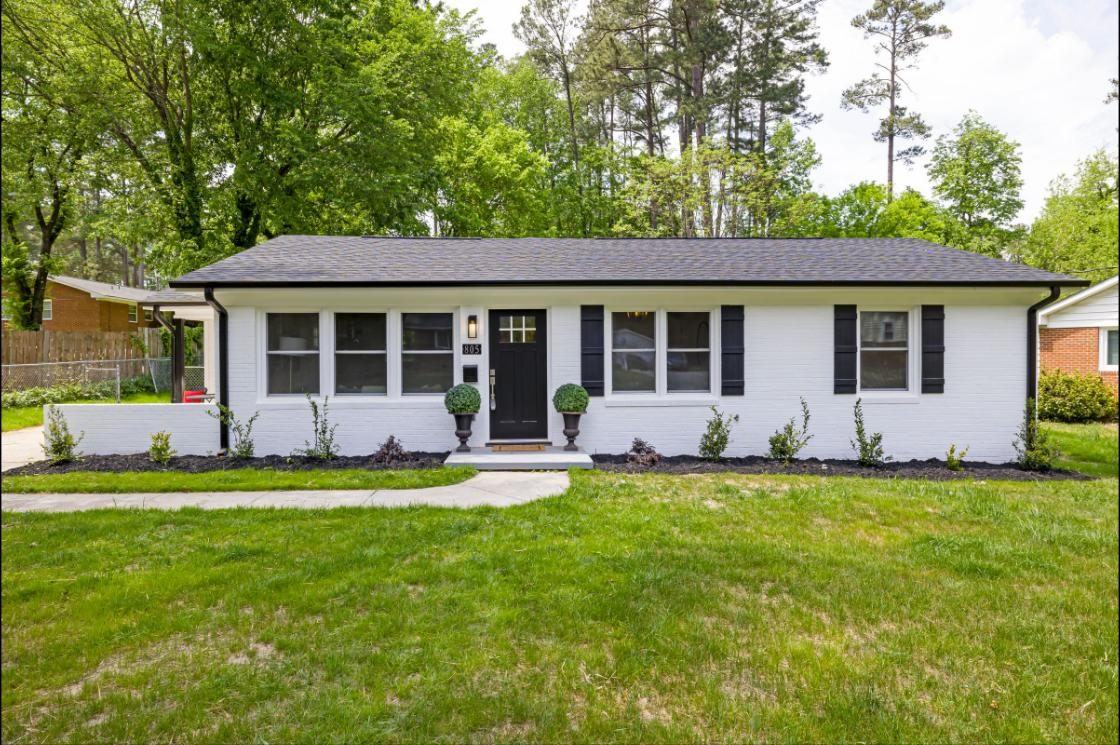 Single-storey painted brick ranch house with black shutters set back behind mature trees
